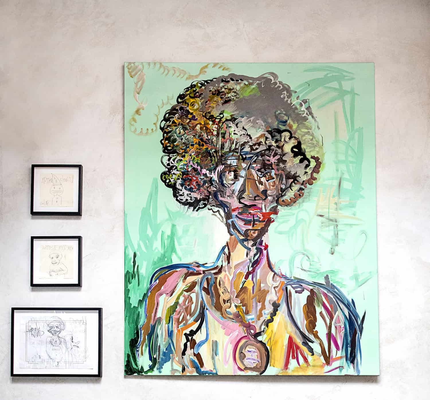 Large abstract painting of a person hanging surrounded by, six hand-drawn works of art, and two sepia toned photos. All are hung on a textured white wall.