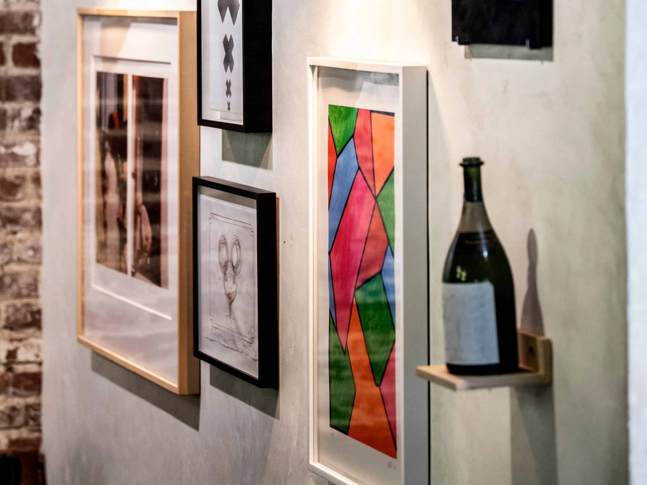 Wall of artworks including a bottle of champagne at Manuela