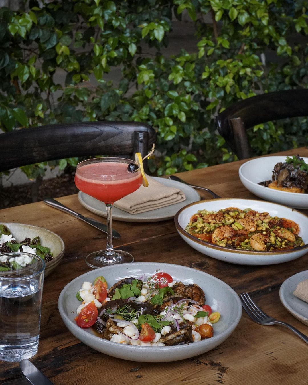 Outside table full of dishes brightly colored dishes and a red cocktail in the middle of the table