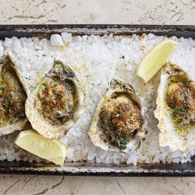 A tray of barbecued oysters dressed with Jimmy Nardello butter, parmesan, breadcrumbs and served with lemon wedges.