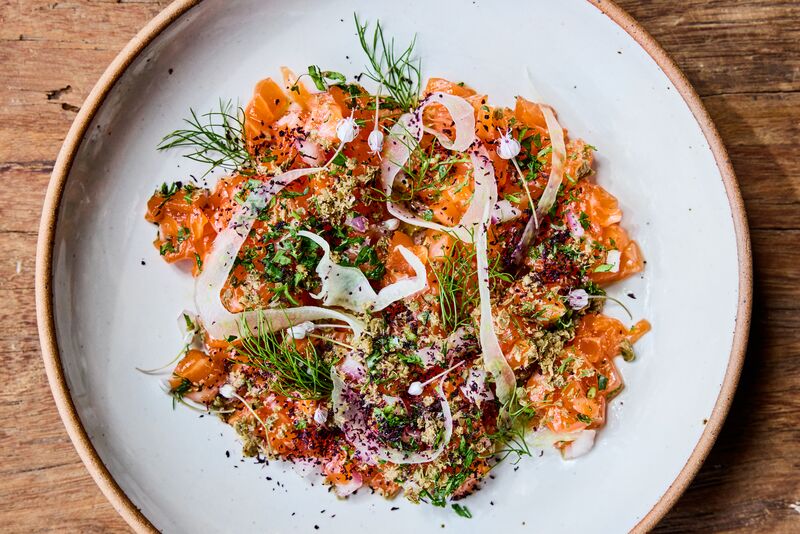 A plate of trout tartare topped with shaved fennel, herbs, and a sprinkling of spices.