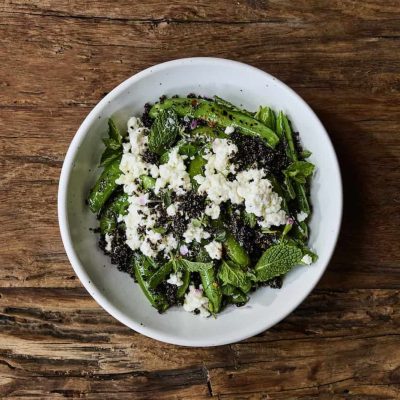 A white bowl full of snap peas garnished with fresh Mint leaves and a white crumbled cheese