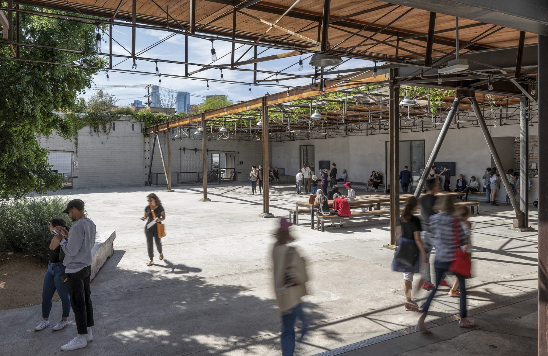 A large, cement outdoor courtyard with a few long communal tables and people walking around.