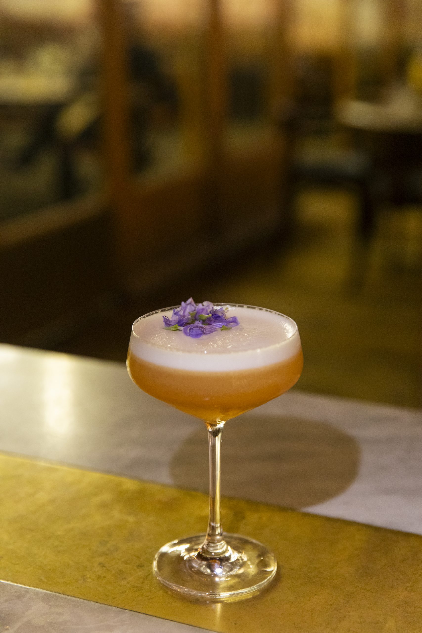 shaken cocktail in a coupe glass with purple flower garnish