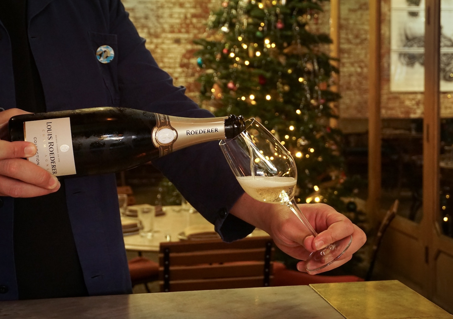 A man pouring Champagne into a wine glass with Christmas tree in the background.