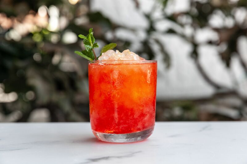 Valentine's cocktail with herb garnish in a rocks glass sitting on a white table top