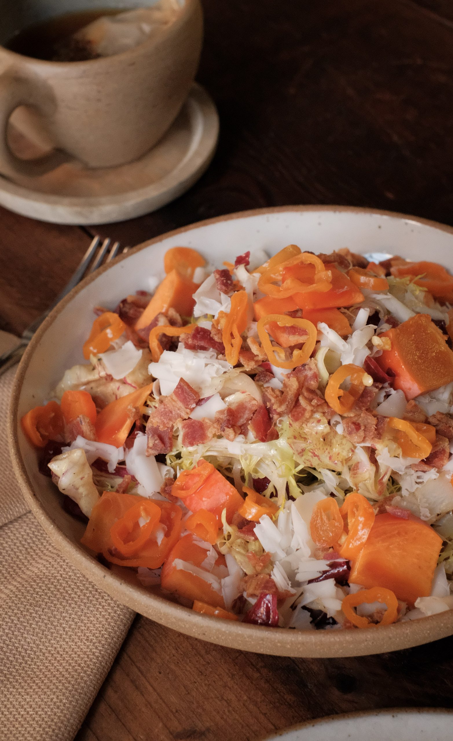 A colorful chicory salad dressed with persimmon, cheese, and bacon crumbles served in a beige bowl.