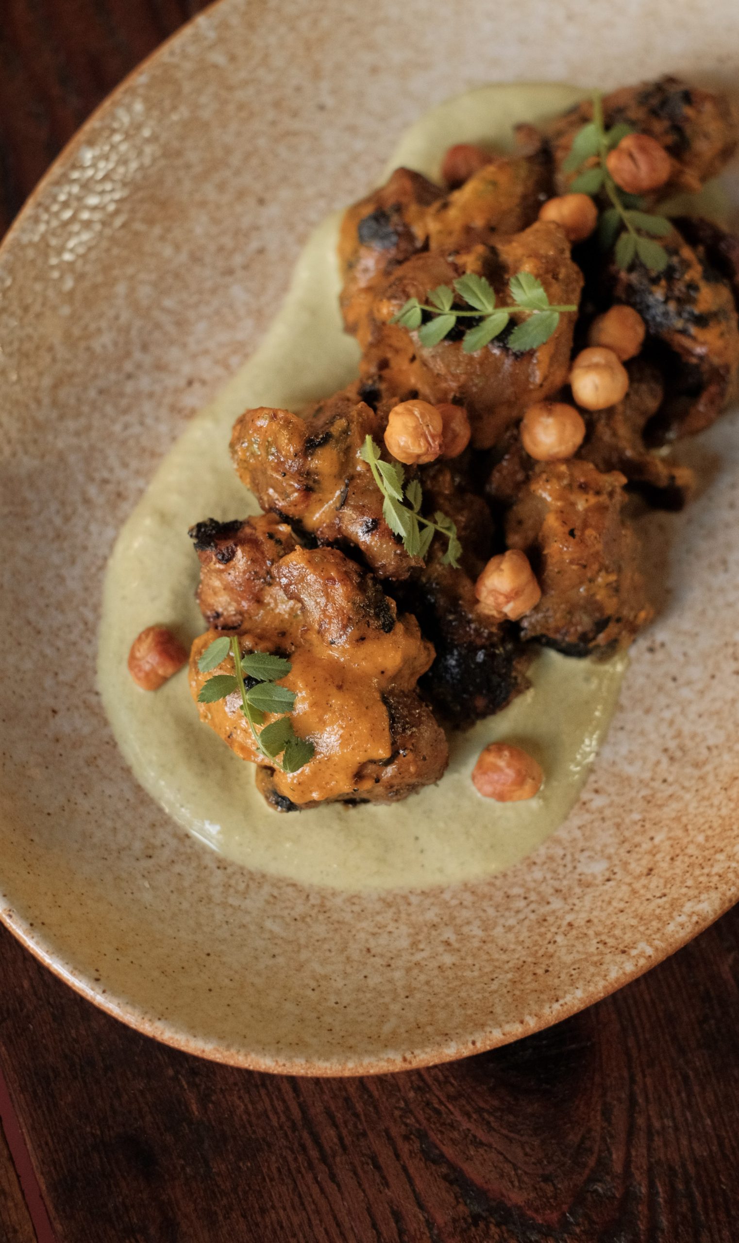 grilled sunchokes with garbanzo beans, covered in a brown curry sauceDish is garnished with cilantro and sits in a textured bowl over a cream sauce.