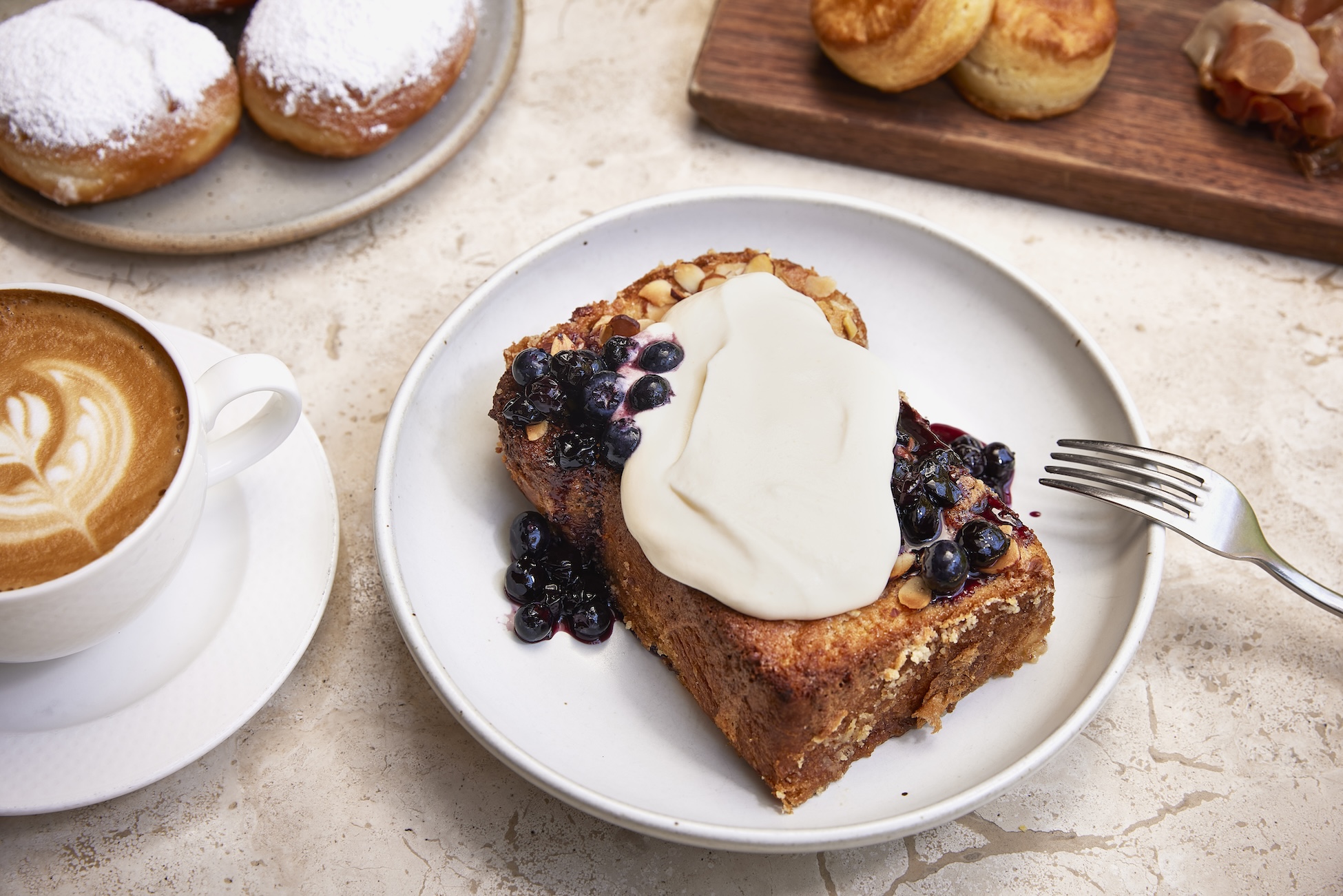 A thick piece of french toast on a round white plate dressed with cream and cooked blueberries.
