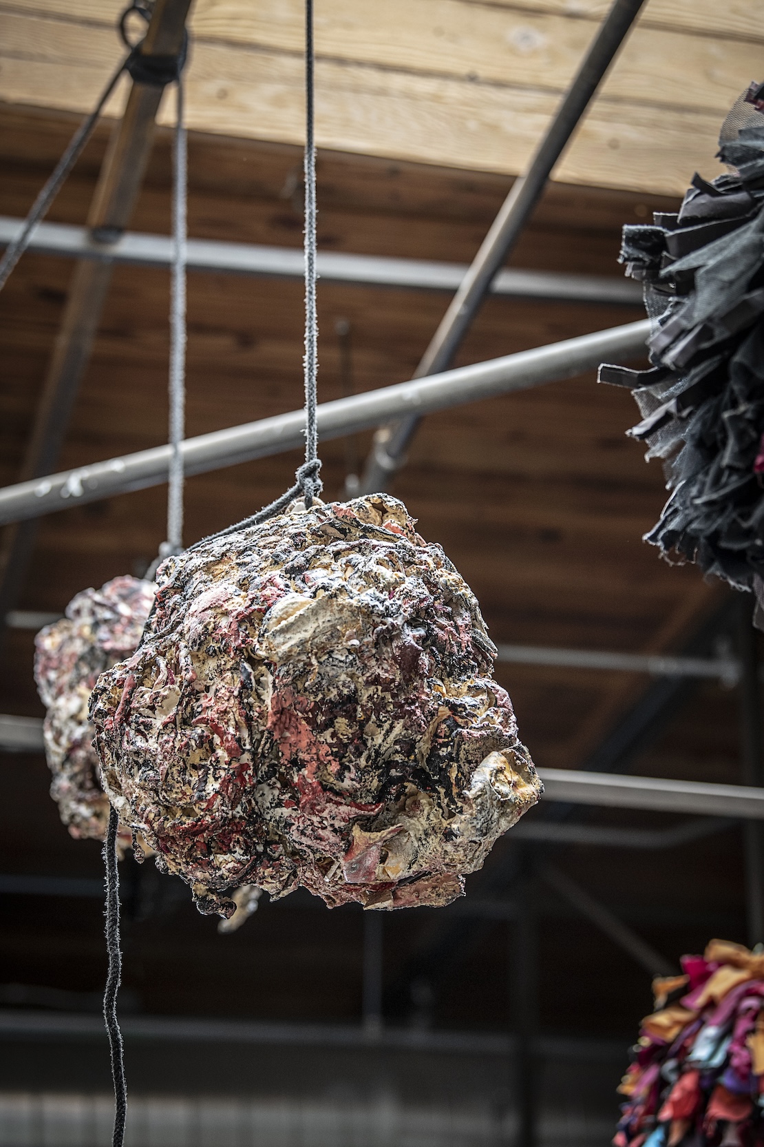 A textured white, black, and pink sculpture hanging from the ceiling by a rope that looks like a rock.