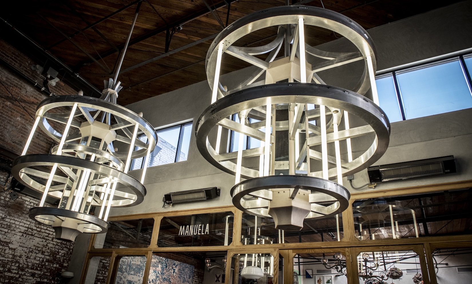 Lighting fixtures in Manuela hanging from the ceiling. Fixtures are made up of metal circles with long strips of light connecting them. Art detail: Paul McCarthy (b. 1945) Crown 2003 Aluminium, fluorescent tubes, mirrors, wood