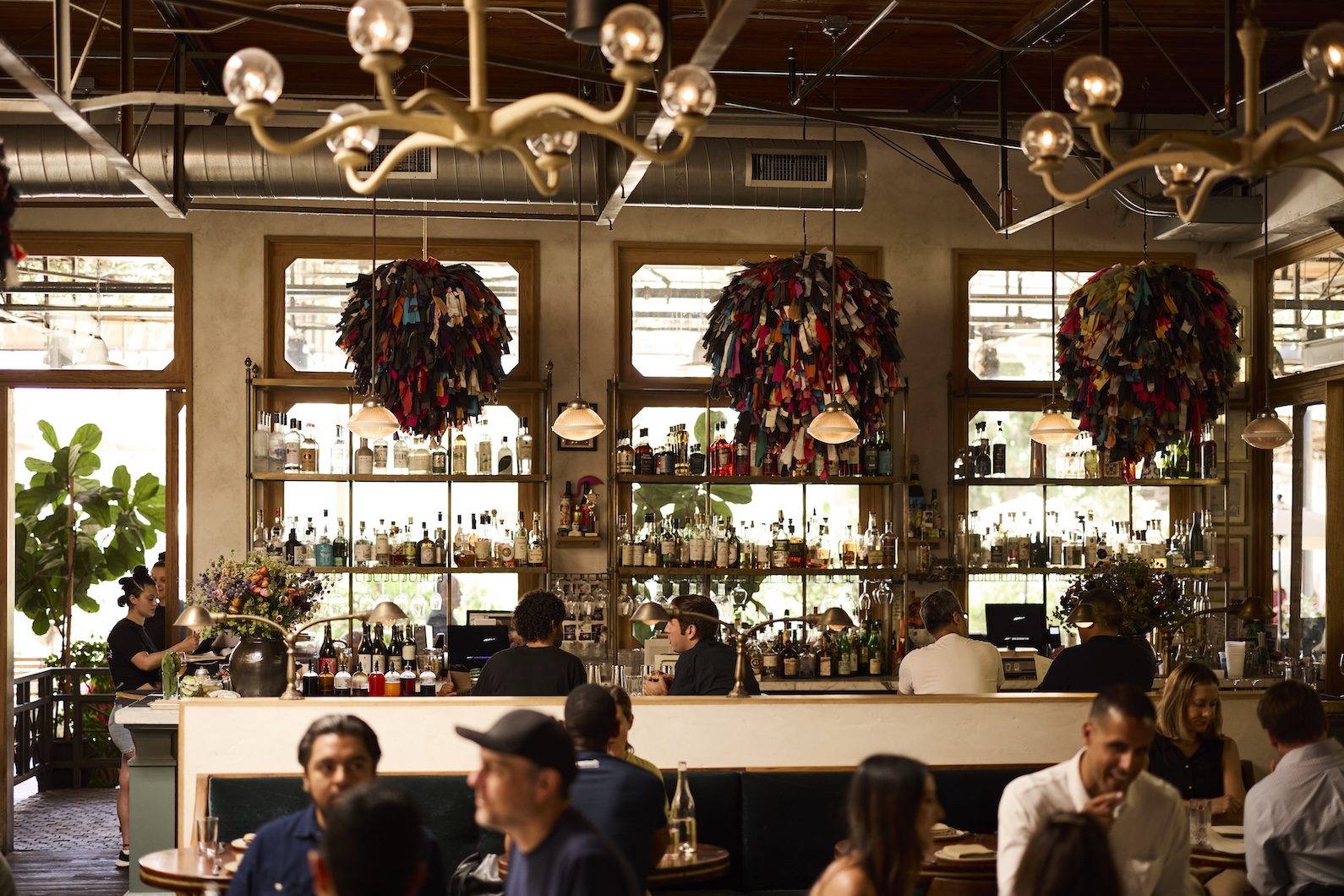 People sitting and dining in a restaurant with a metal chandelier and round colorful sculptures hanging above them