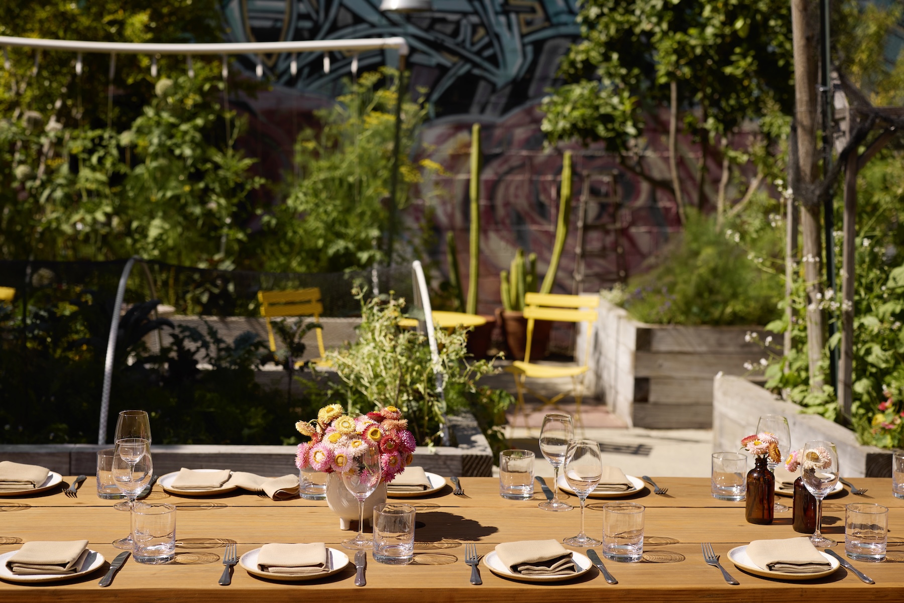 A long table set for dining with pink floral arrangements and a green garden in the background.