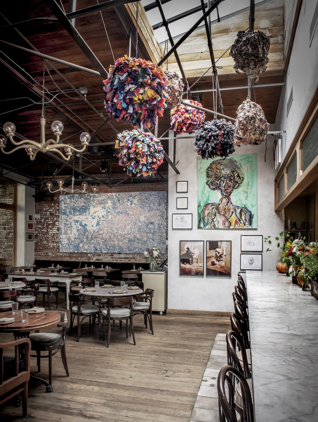A kitchen dining room with various works of art on the walls and round colorful sculptures hanging from the ceiling.