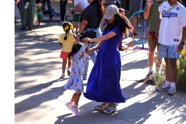 A mother and child dancing in a courtyard surrounded by other kids and parents dancing