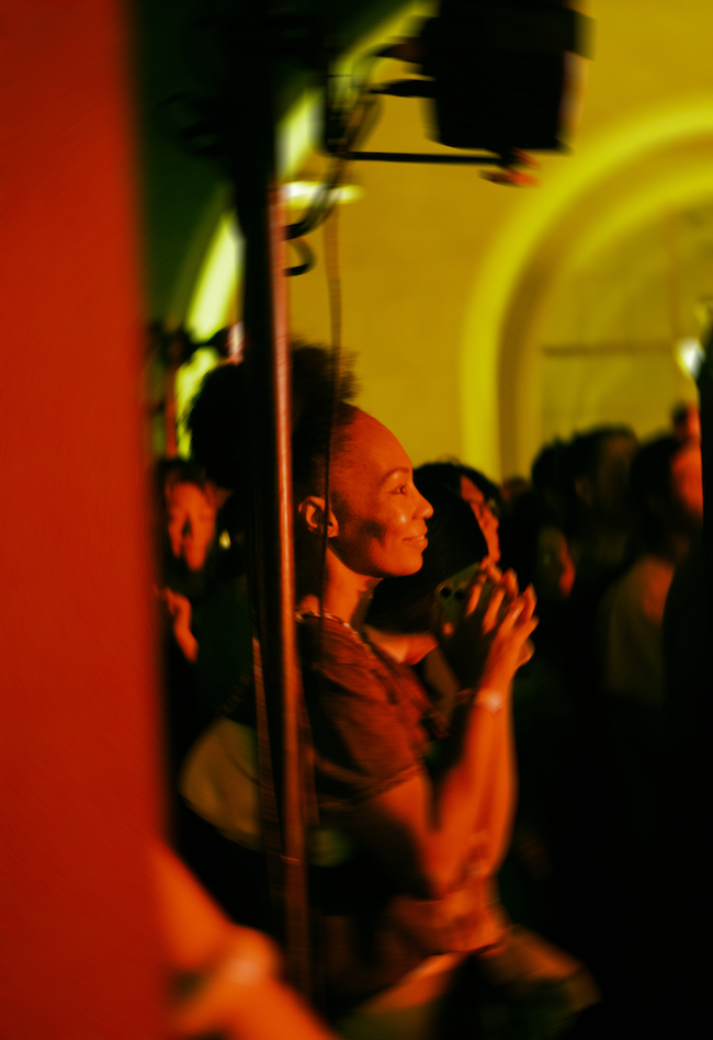 Woman lit in an orange light smiling slightly listening to music.