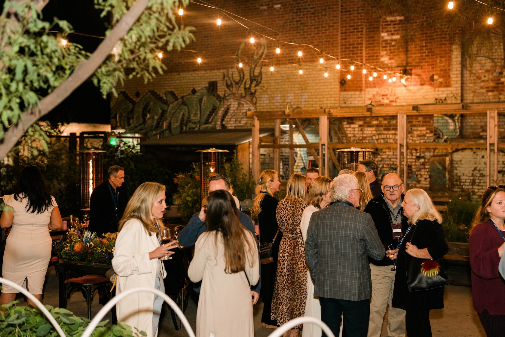Group of people standing under a string of lights socializing at a party in Manuela's garden.