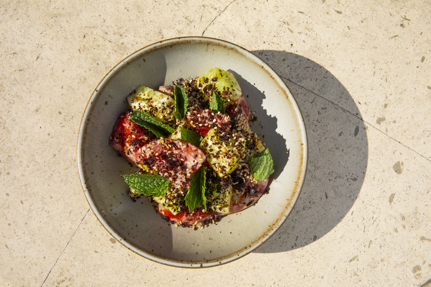 Beige plate on a beige table with red and yellow tomatoes garnished with basil and Aleppo pepper