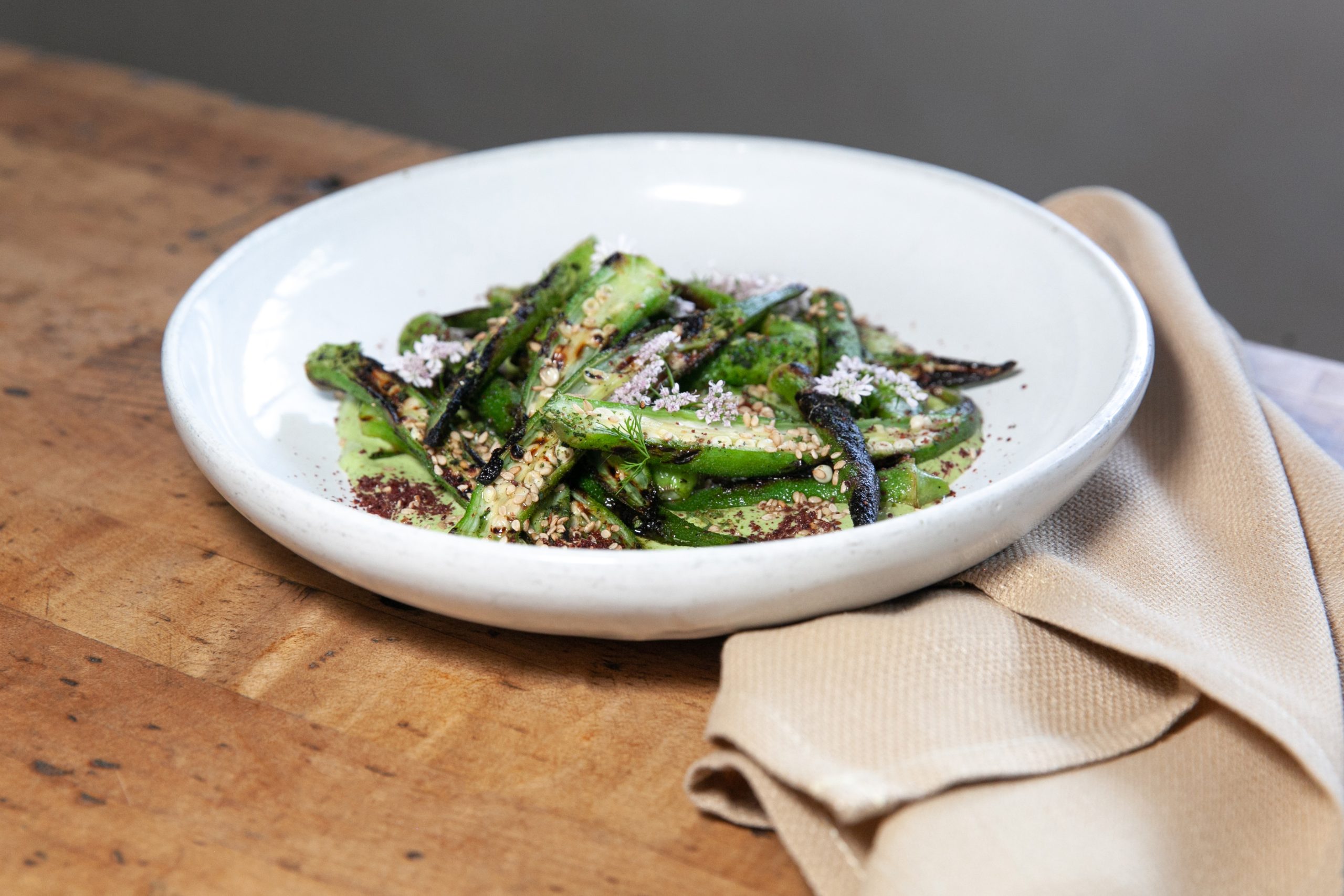A white plate full of cooked green okra slices on top of a light green sauce.