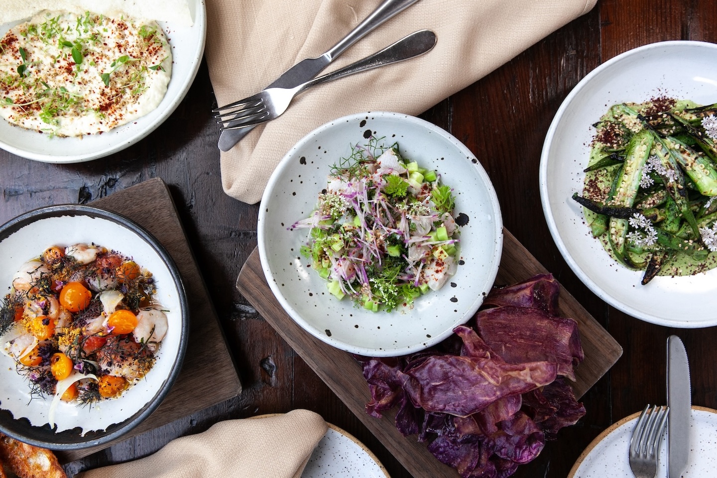 A variety of plates with food sitting on a wooden table with napkins and forks