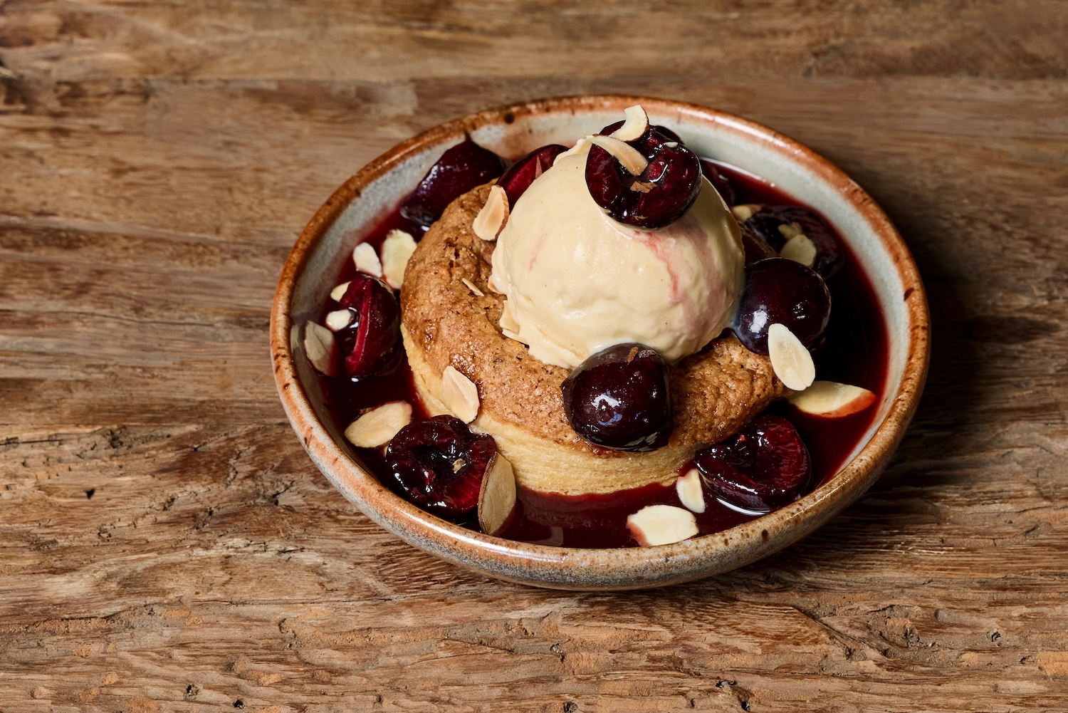 A small plate with a dessert tart covered in vanilla ice cream, dark cherries, and almonds