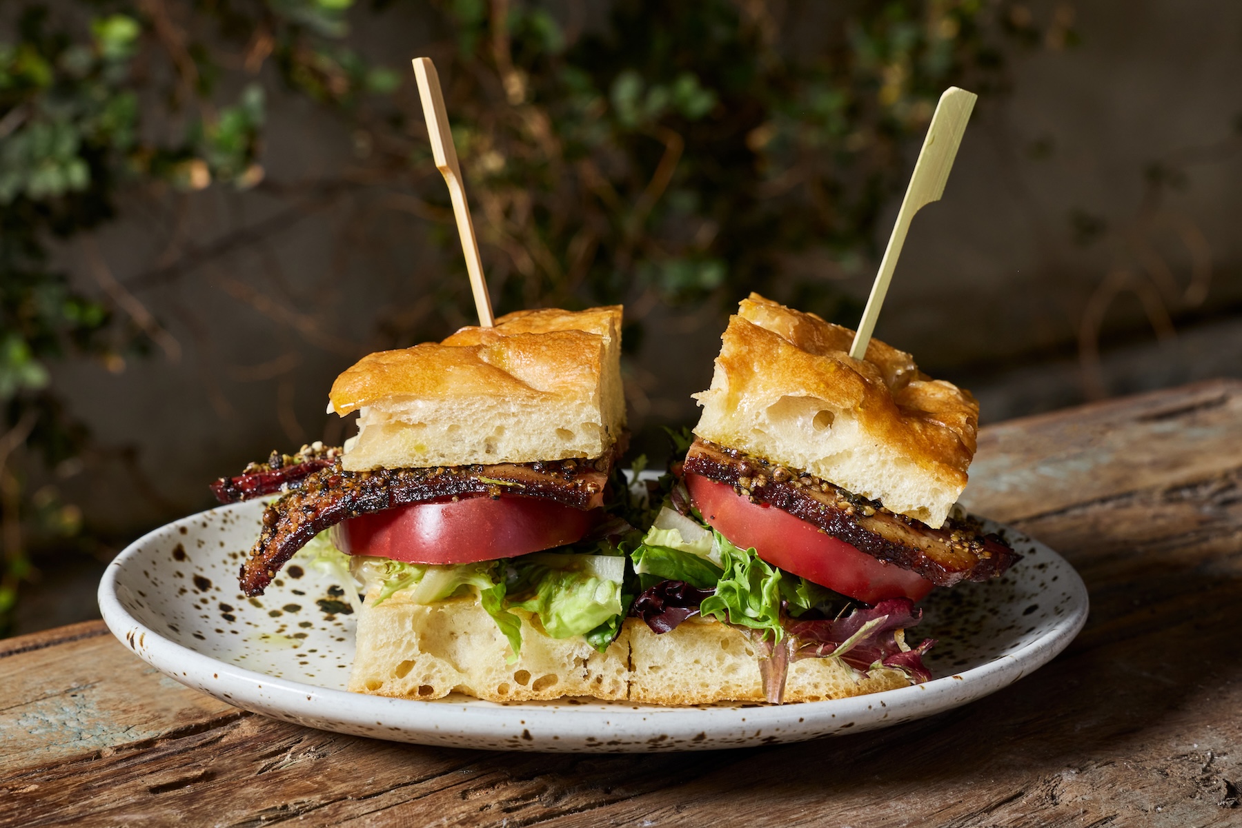 A plate with a focaccia sandwich full of bacon, lettuce, and tomato