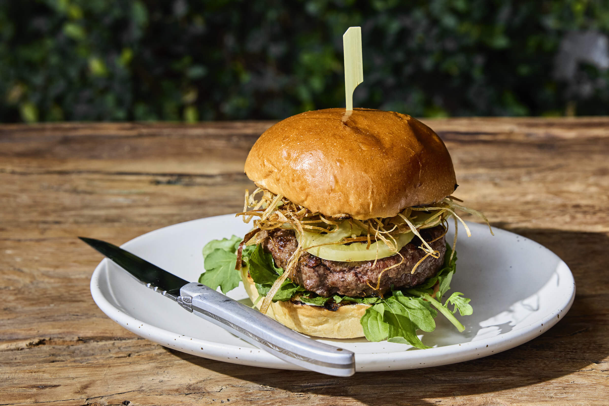 The signature venison burger on a wooden table with a knife beside it
