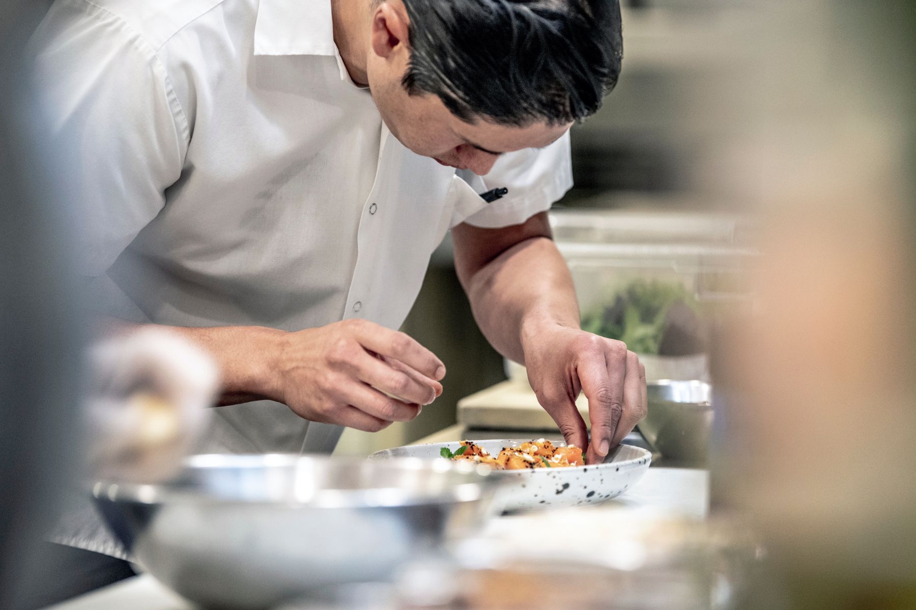 Chef carefully garnishing and plating a dish in a professional kitchen, focused on adding finishing touches before service.